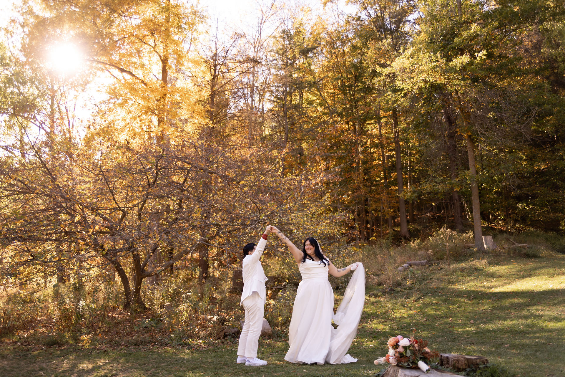 bride spinning around holding her dress and her brides hand in front of trees and a setting sun