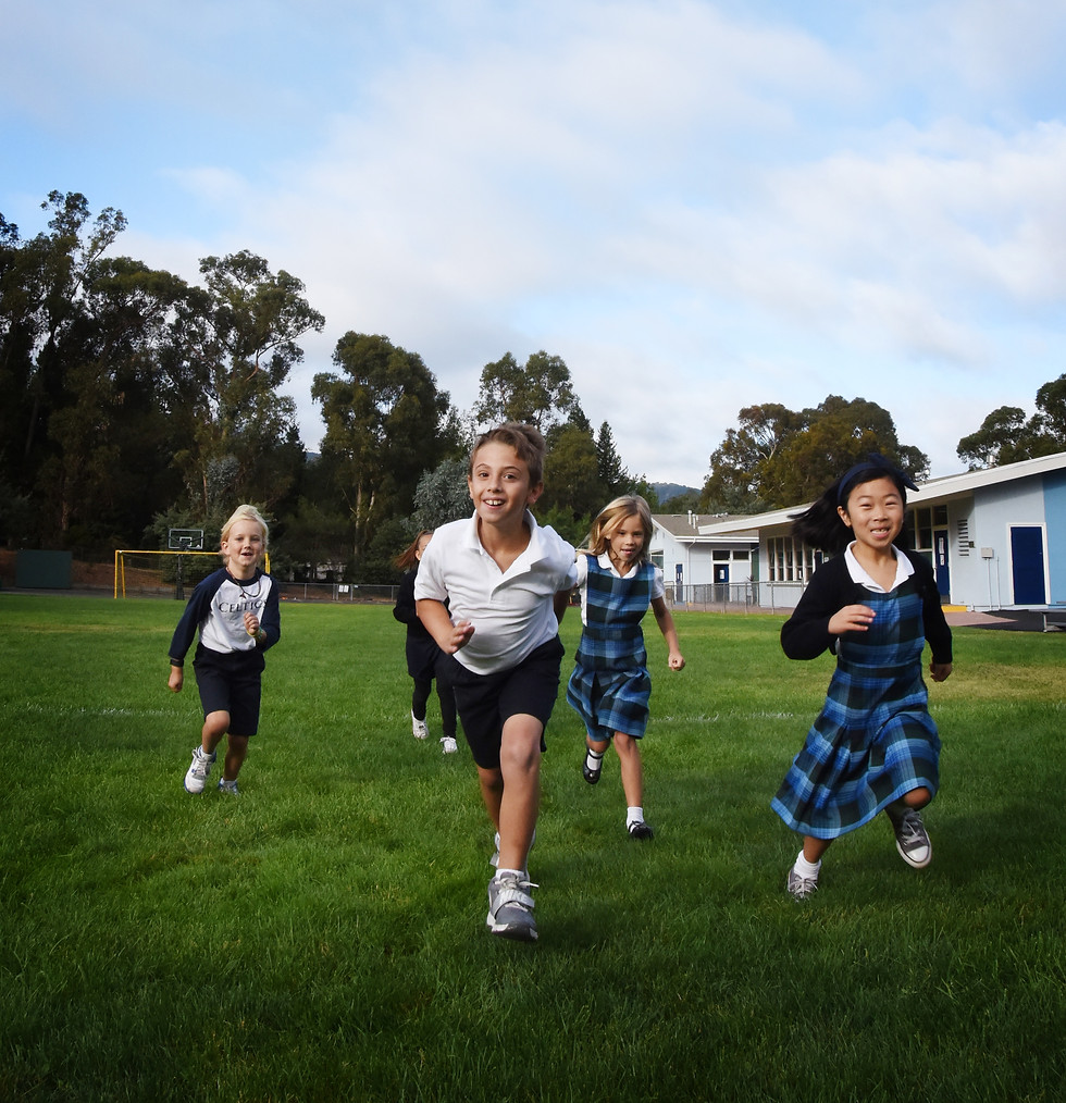 A link to the Saint Nicholas Catholic School Social Emotional Learning Page. The photograph shows elementary school students happily running across a large field during recess.