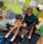 A link to the Social-Emotional Learning page. The image shows two eigth grade boys read to a transitional kindergarten student at Saint Nicholas Catholic School.