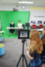 A middle school girl takes a video of two other students sitting in front of a green screen. Saint Nicholas Catholic School has a fully equipted Technology Lab.