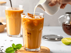 two glasses of thai iced tea with someone pouring a milk