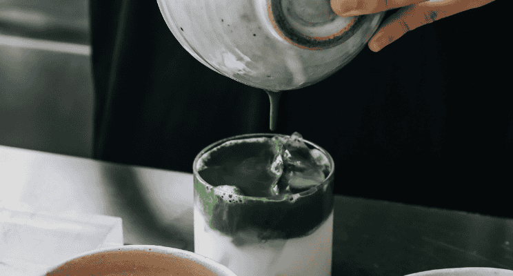 a person's hand shown as pouring a matcha into a glass