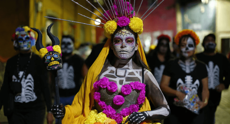 a woman in traditional dia de los muertos makeup leading a parade of people during the dia de los muertos commemoration