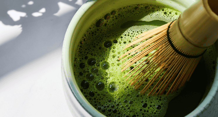 matcha mixture in a bowl with a matcha bamboo whisk