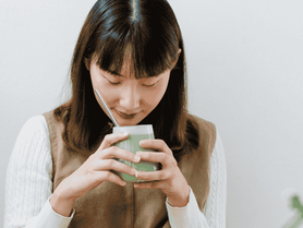 asian woman smelling the cup of matcha she's holding
