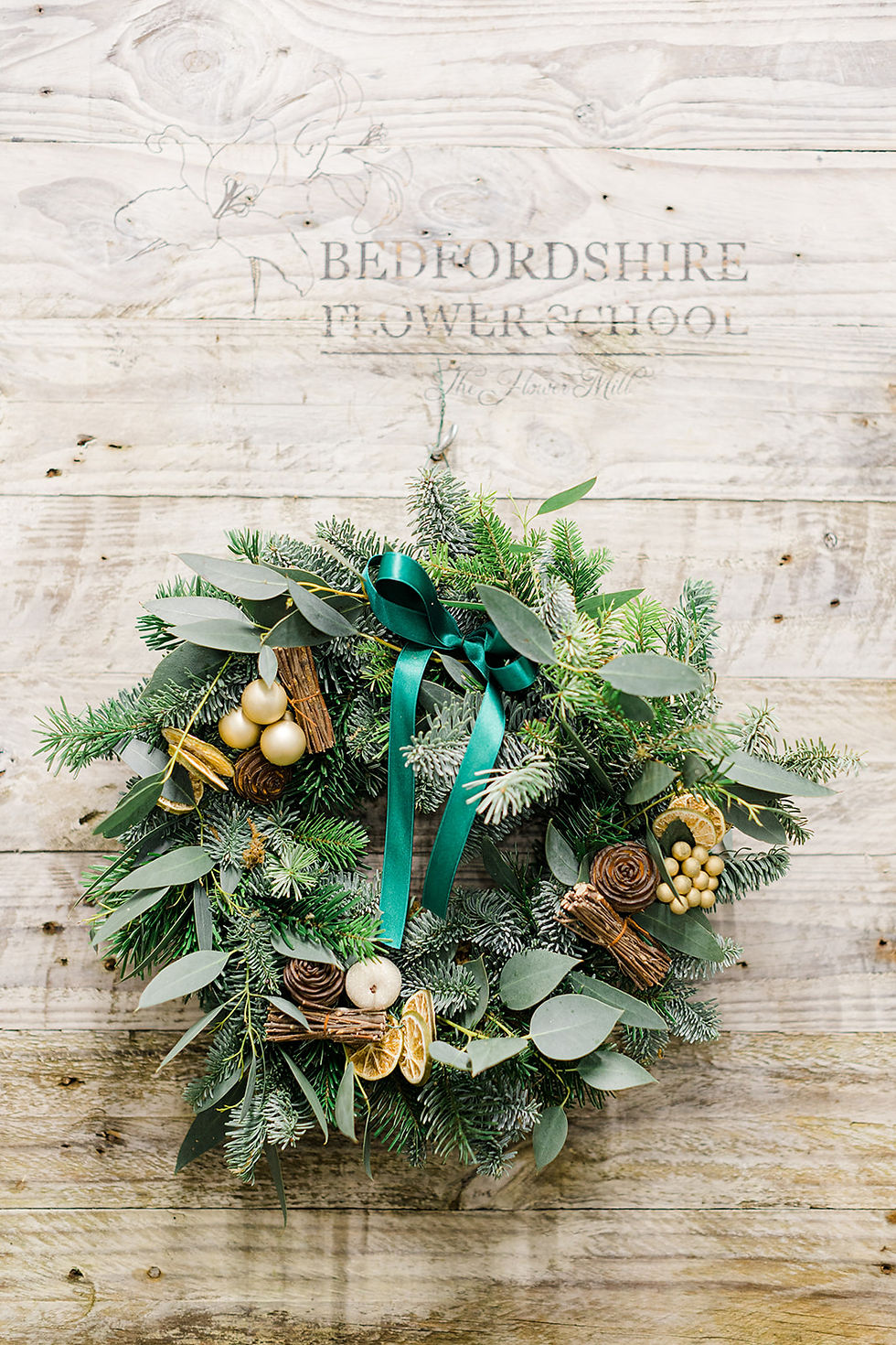 Transform a simple Christmas wreath by adding fresh foliage, seasonal decorations like pinecones and dried oranges, luxurious ribbon, and refreshed elements for a vibrant, festive display.