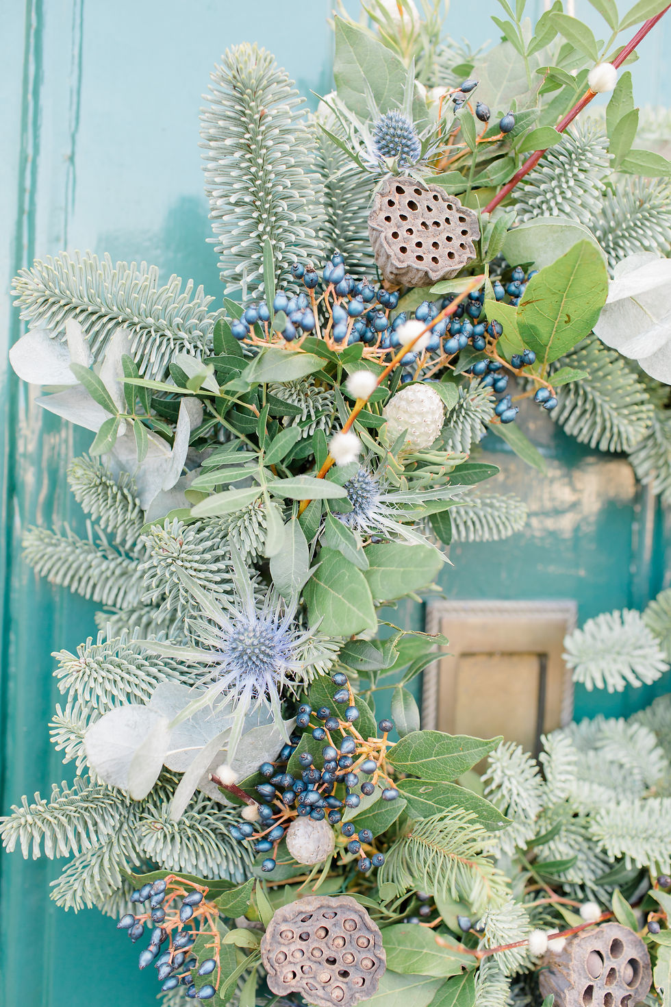Learn how to make your Christmas wreath better with expert tips, including adding extra foliage, festive decorations like pinecones and dried oranges, and incorporating twinkling lights. This handmade Christmas door wreath pictured includes fresh thistles, lotus heads and blue berries.