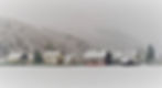 Snow-covered houses in a quiet village at the base of a frosty mountain, with foggy gray skies and still winter mood