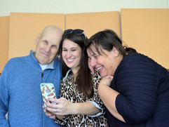 An elderly man and two women smiling at a phone together