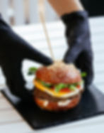 Person wearing gloves holding a gourmet burger on a black tray. 