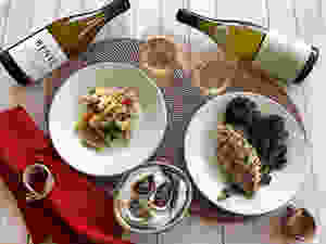 Two bottles of chardonnay on their side next to wine glasses and dinner plates filled with food.