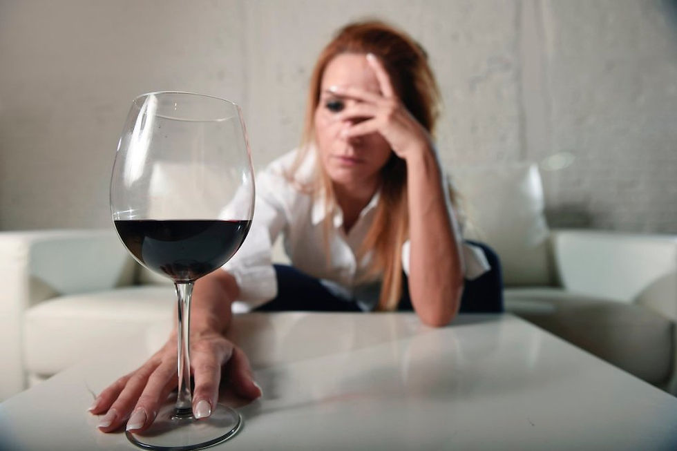 Woman holding her head with a glass of red wine in front of her.