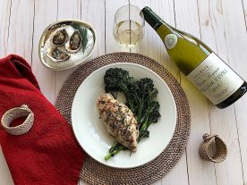 Bottle and glass of Chablis next to oysters and plate of roasted herbed chicken and roasted broccolini.