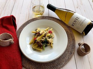 Bottle and glass of oaked chardonnay next to plate of chicken penne alfredo.