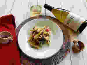 Bottle and glass of oaked chardonnay next to plate of chicken penne alfredo.