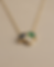 Close-up of a delicate gold chain necklace with a trio cluster of emerald, green sapphire, and brilliant-cut diamond