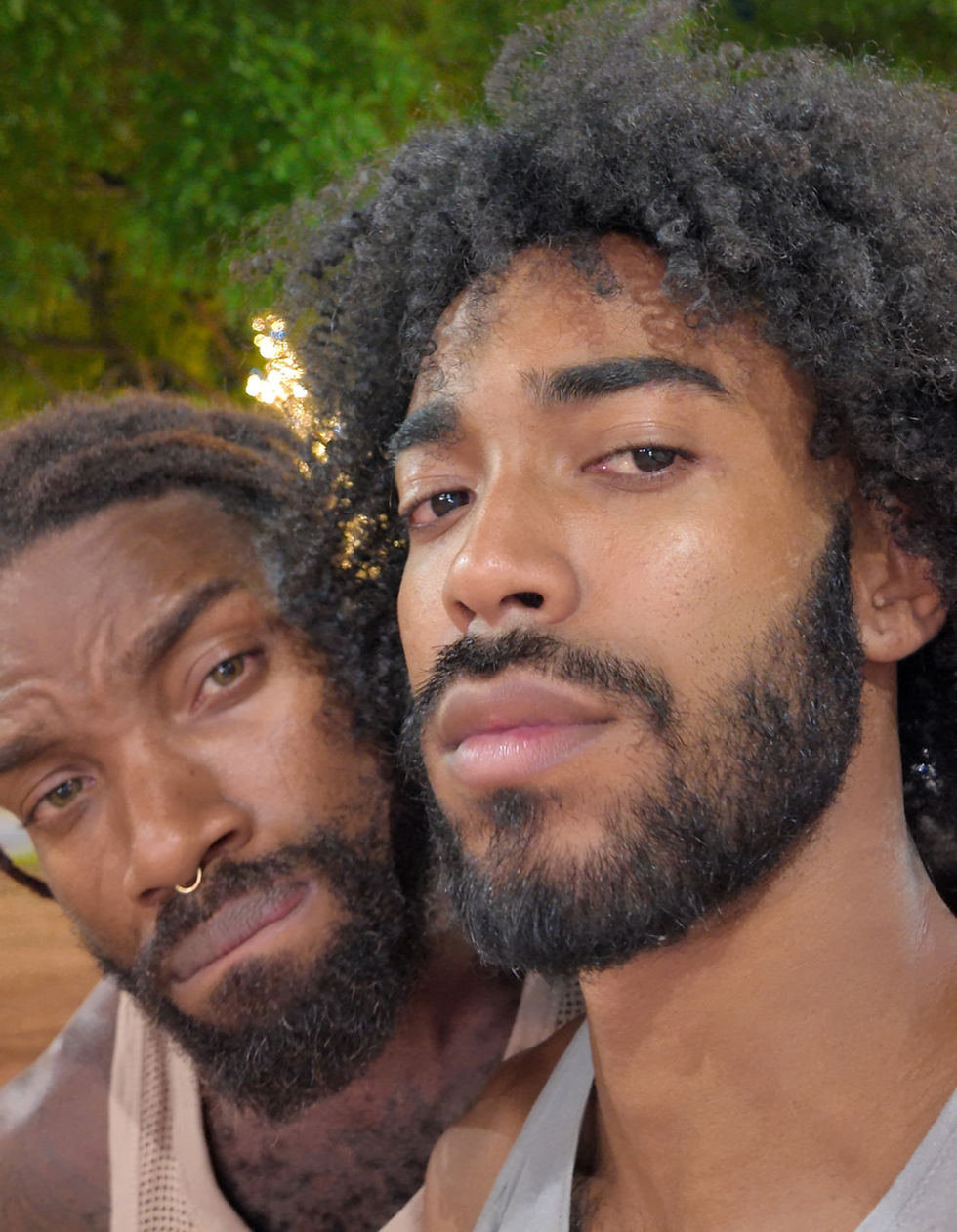 two gay black boys smiling at the camera in front of a Christmas tree and lights