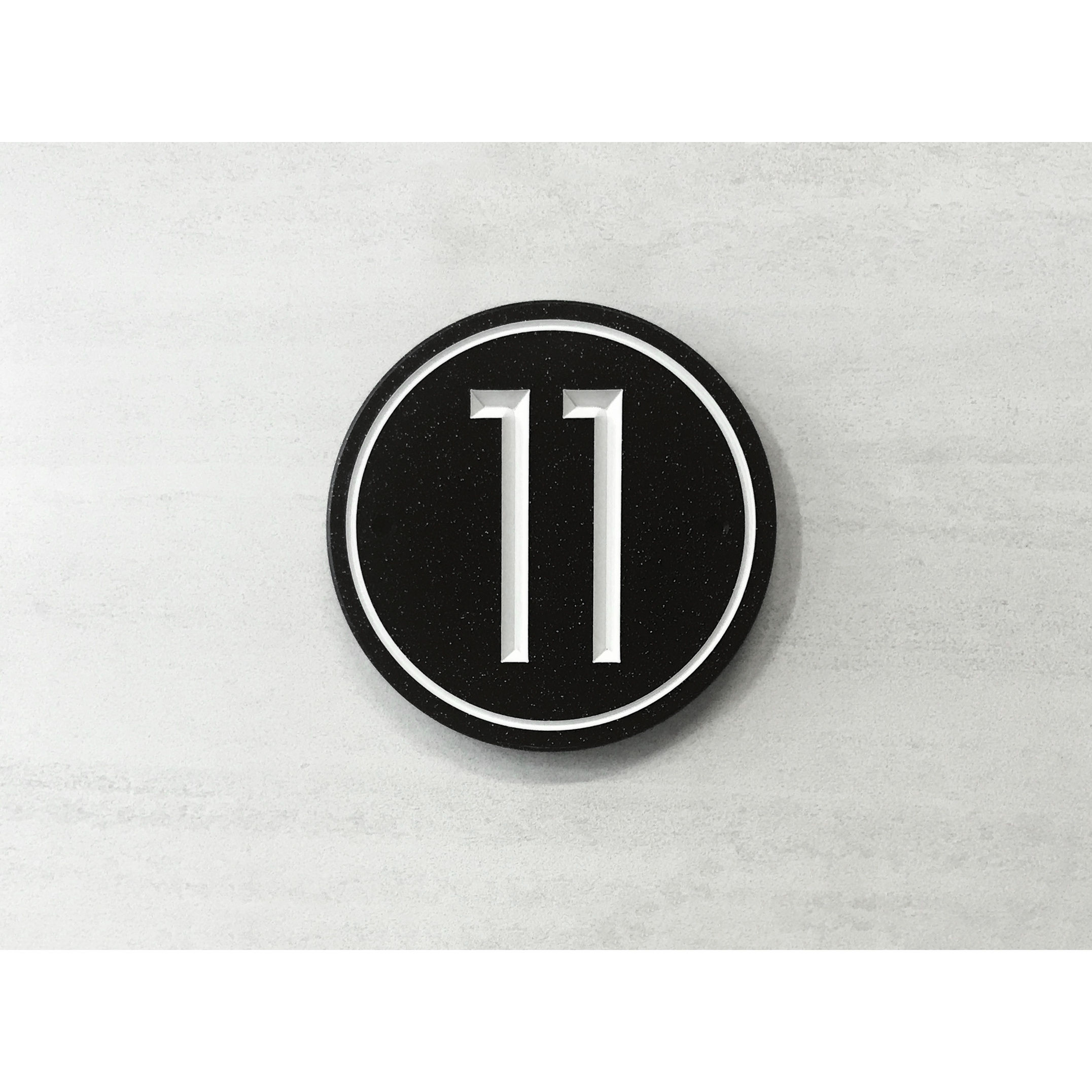 Circular address plaque featuring V-carved house numbers on a weatherproof, stone-look solid surface material.