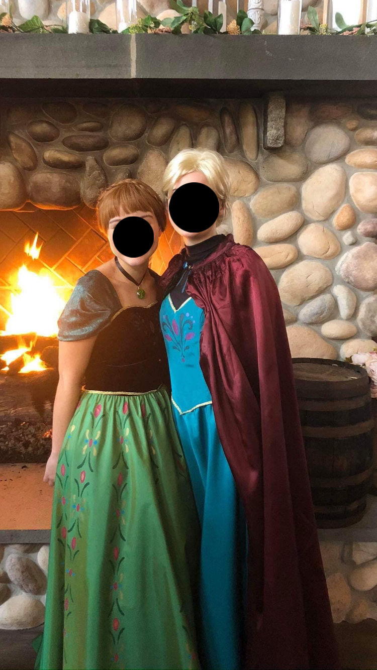 Two people in Anna and Elsa costumes by a fireplace