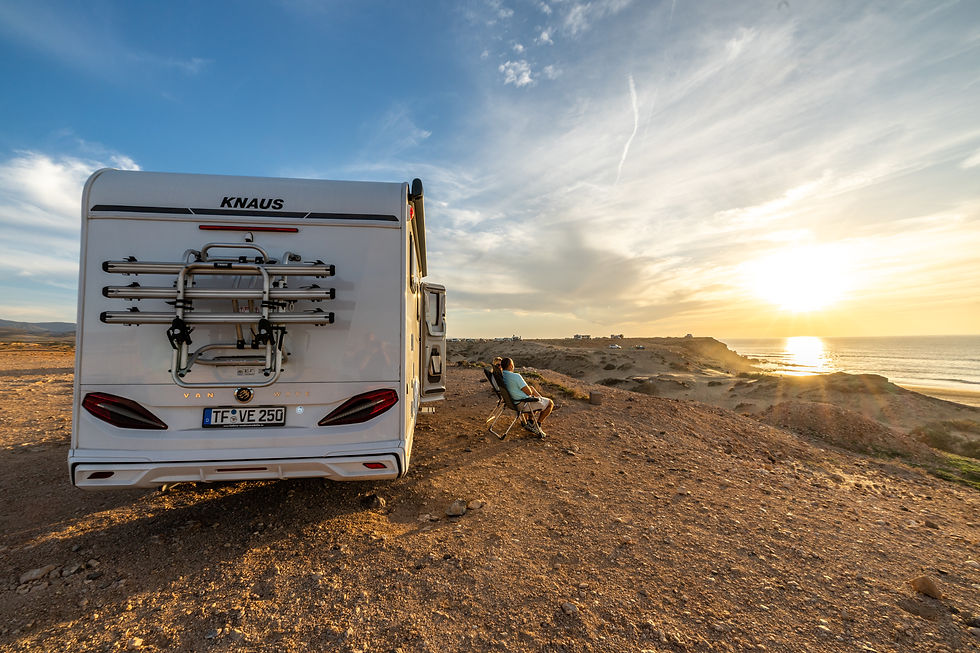 Couple enjoying dinner on outdoor camper furniture beside a low-profile Knaus campervan on a rugged Tenerife coastline during sunset.