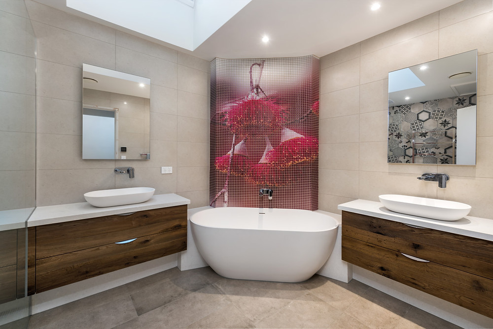 A semi freestanding bath sits between 2 vanities and the bath has a custom tiled mural across the corner. - The clients own photograph converted to tiles