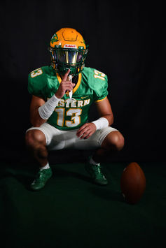 A high school football player crouches with a finger to his lips in a hush motion