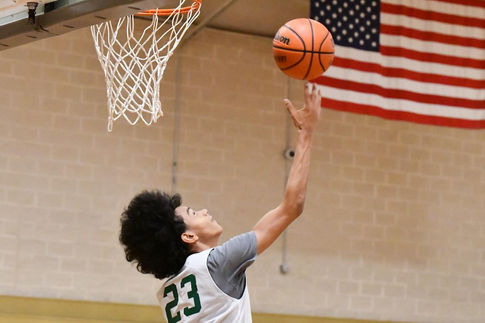 A young man with an afro goes up to dunk the basketball behind him into the hoop. The ball has just left his right fingertips.