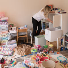 Blonde lady tidying up a messy playroom