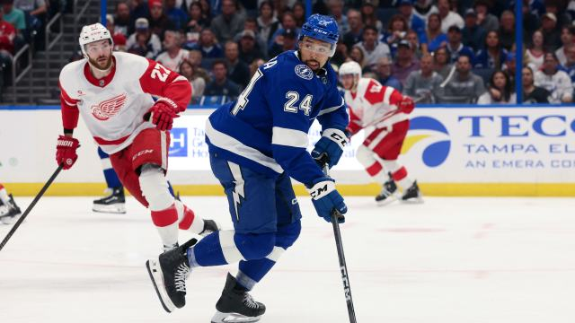 Matt Dumba playing for the Tampa Bay Lightning. A Detroit Red Wings player in the background is watching him.