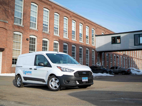 A modern white cargo van with the Empire Studios logo on a sliding door, parked in an industrial, all-brick building complex.