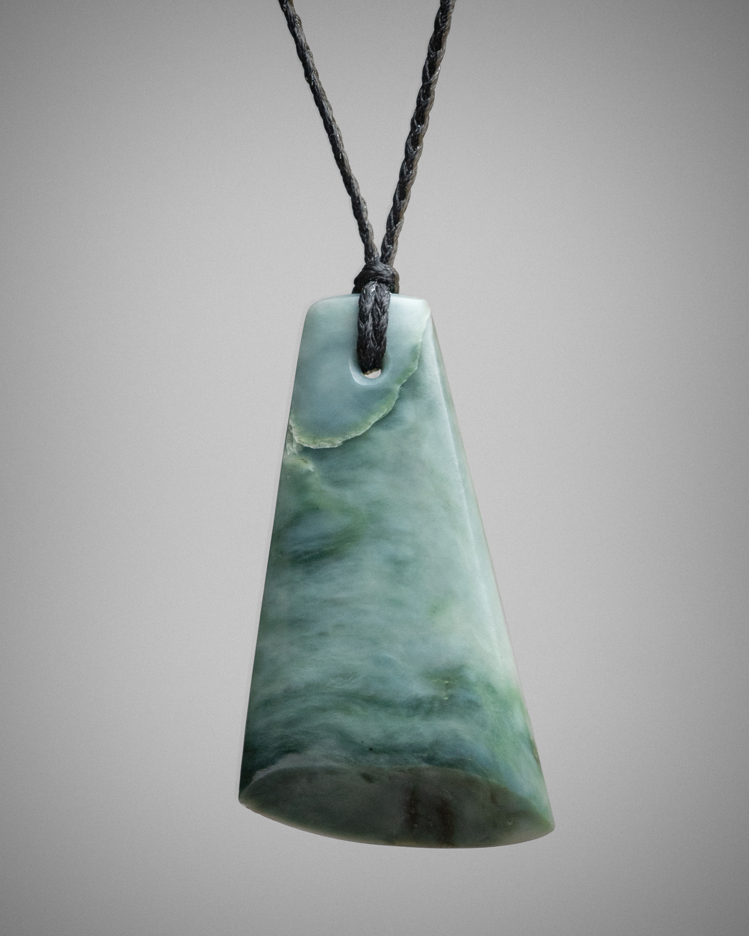 Blue nephrite adze pendant on black cord, front view with blue-green layers