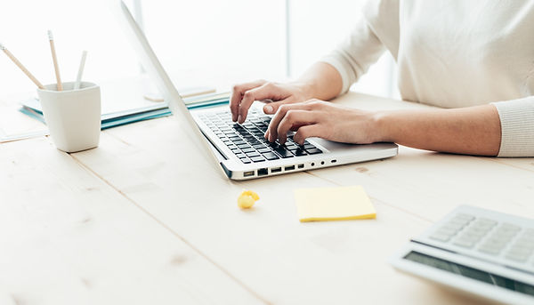 Woman in sitting at white desk and typing on a laptop