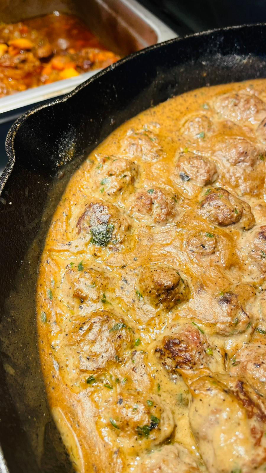 Gourmet meatball served in a rich, flavorful sauce inside a cast iron pan, showcasing an elegant and rustic culinary presenta