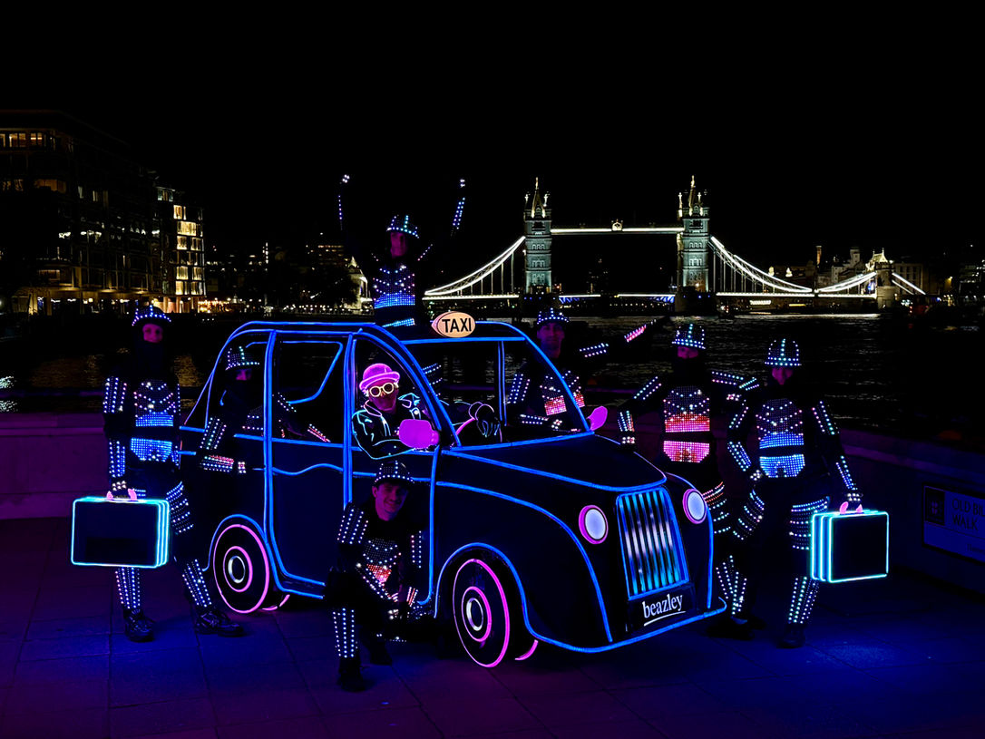 THE BLACKOUTS performen eine LED-Show in London mit leuchtendem London-Taxi vor der Londoner Tower Bridge.