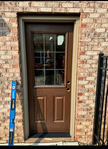 Wood-look glass-panel door in a brick opening during installation, with a level beside the frame