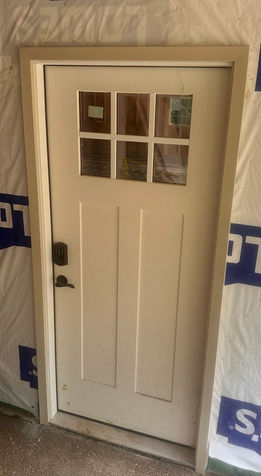 Light-colored six-pane entry door with dark handle and keypad lock during construction