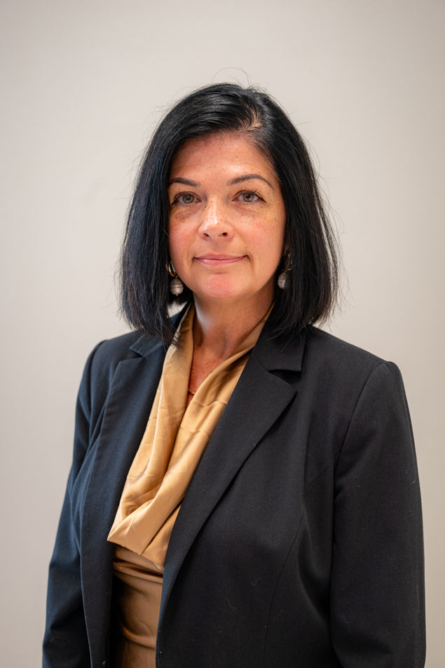 Dramatic studio headshot of a professional in a dark blazer and scarf against a black background