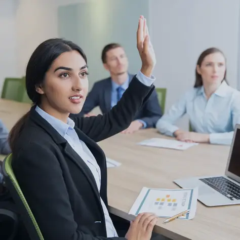Professional team engaged in a discussion, with one employee confidently raising a hand to share input—illustrating a Voice of the Employee culture where feedback, transparency, and psychological safety drive engagement and organizational growth.