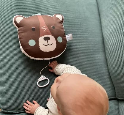 Bébé allongé sur un canapé vert qui attrape le coussin musical ours brun
