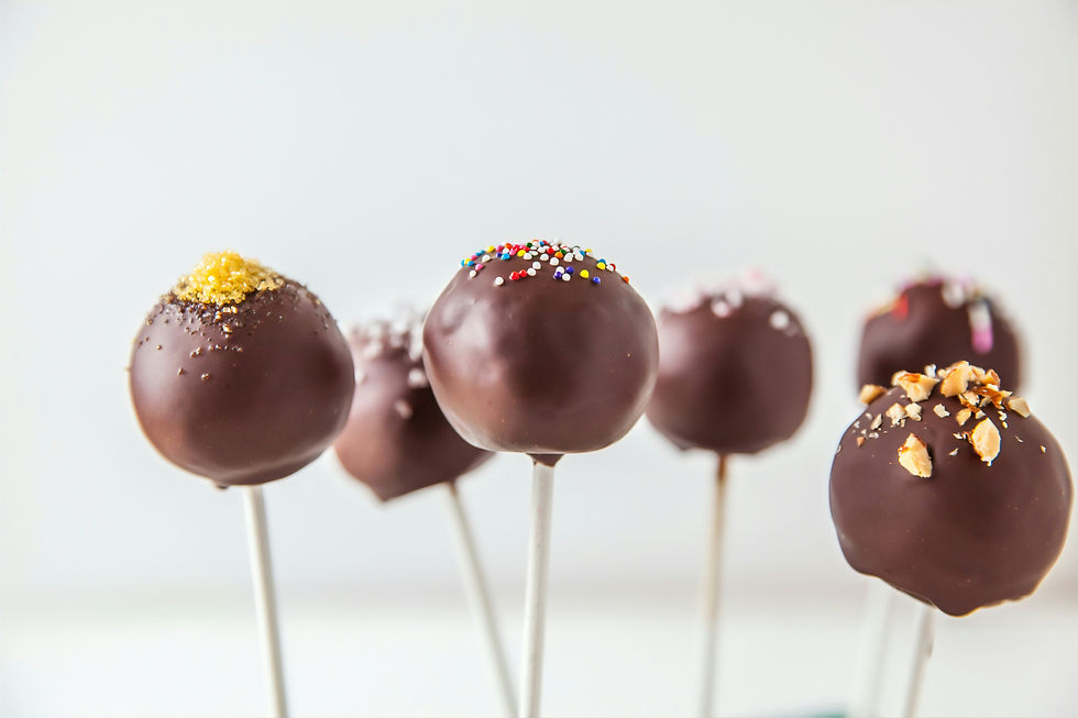 Chocolate cake pops on sticks, coated in dark chocolate with sprinkles and nuts, against a bright white background.