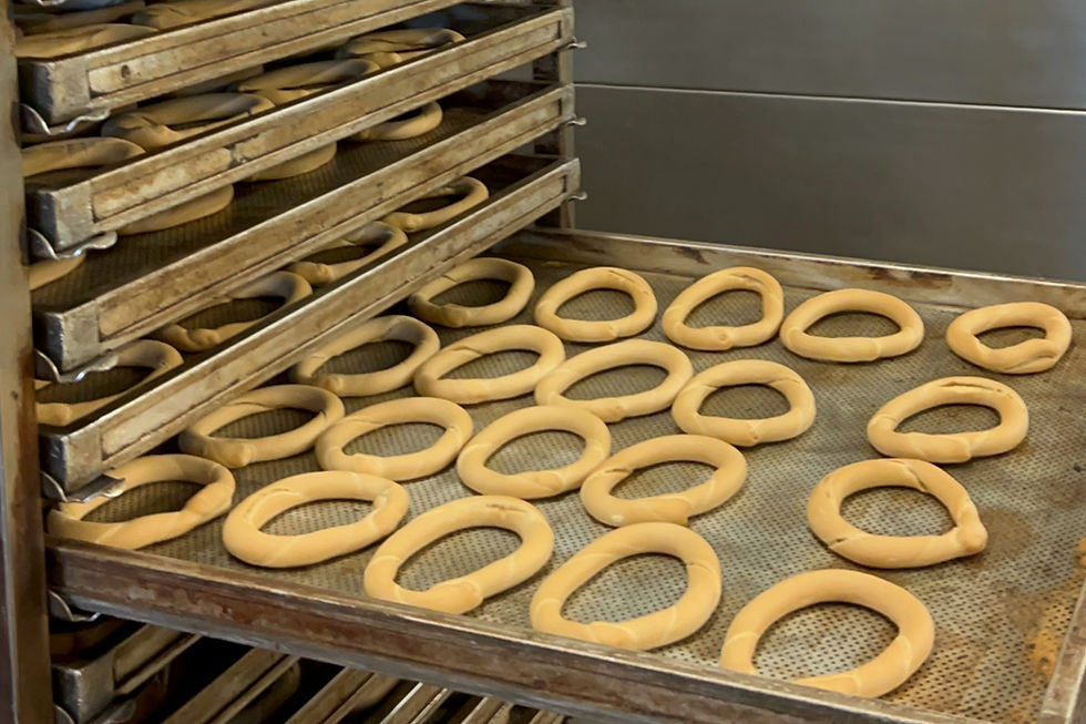 Rows of pale dough rings on metal baking trays in a bakery, stacked rack in a warm industrial kitchen.