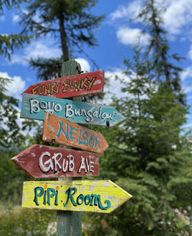 Wooden directional sign pointing to log cabins at Bunkie Land camp, a mountain retreat near Nelson BC
