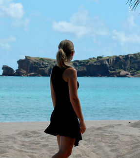 A photo of Rebecca on a beach, facing away from the camera. The ocean behind her is bright blue and looks very tropical.