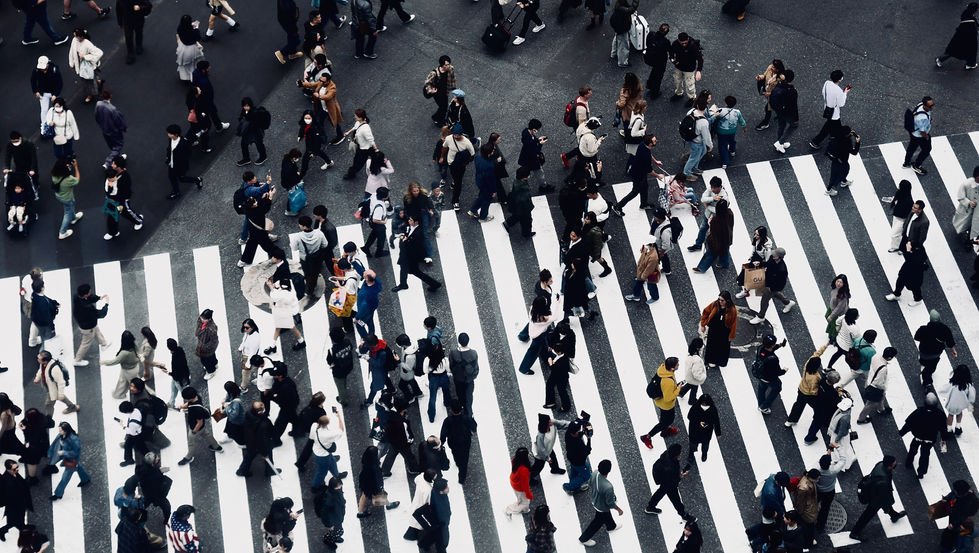 A dense river of movement at the iconic Shibuya Crossing. The top-down perspective flattens the chaos into a patterned rhythm of motion and anonymity.
