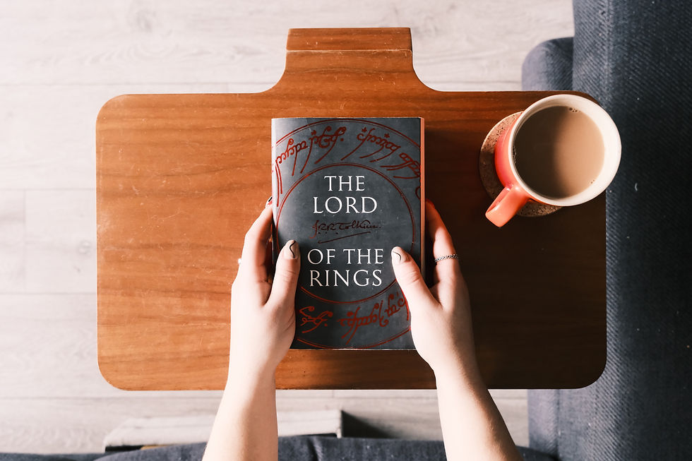 The Lord of The Rings book held in two hands on a table, next to a cup of tea.