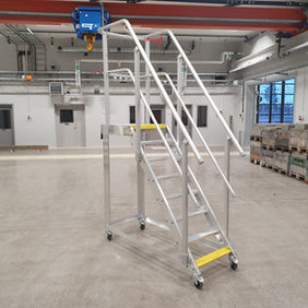 En mobil trappa av smalare variant som står ensam på ett verkstadsgolv.