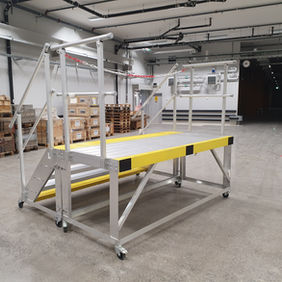 En mobil trappa och en mobil plattform i aluminium som står upsställda tillsammans i verkstadsmiljö