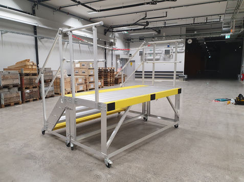 En mobil trappa och en mobil plattform i aluminium som står upsställda tillsammans i verkstadsmiljö