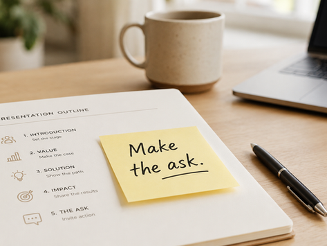 Close-up of presentation notes on a desk with a sticky note that says ‘Make the ask,’ laptop and coffee blurred in background.