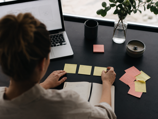 Professional arranging three selected sticky notes in a row on a desk, with additional notes set aside beside a laptop and notebook.